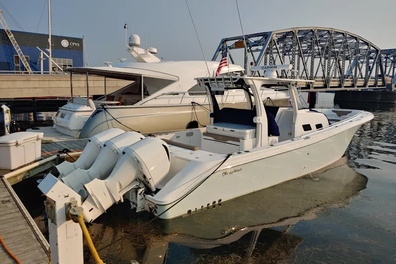 Slide: The Image of 2021 Edgewater 370CC boat docked near a bridge, featuring powerful outboard engines. - 2