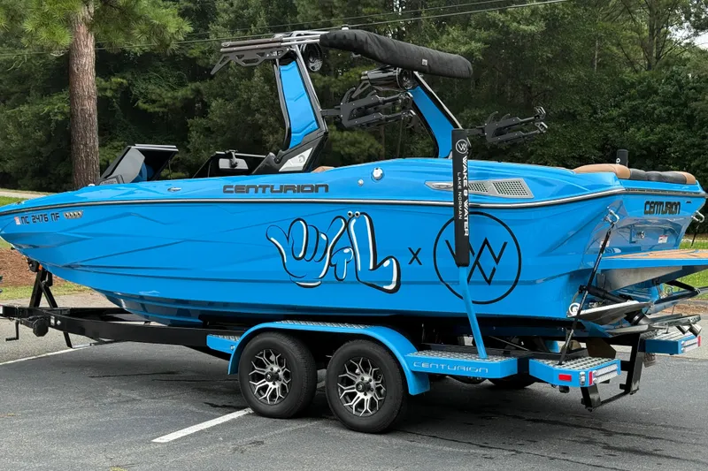 Slide: The Image of 2025 Centurion Nv233 boat in vibrant blue with custom graphics on a trailer. - 24