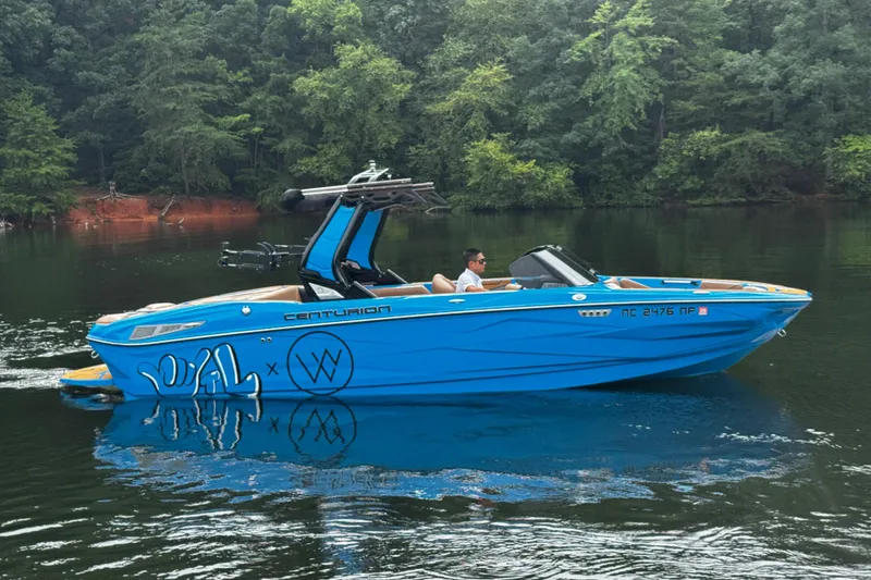 Slide: The Image of 2025 Centurion Nv233 boat cruising on a serene lake with lush forest backdrop. - 4