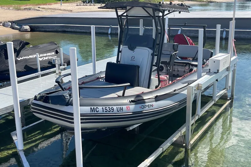 Slide: The Image of 2019 Zodiac Open 7 boat docked on a lift, with clear water and shoreline background. - 2