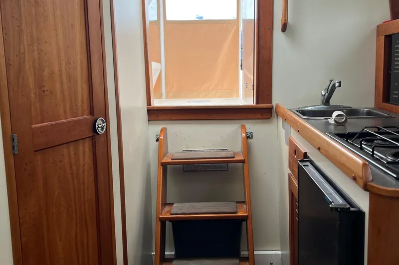 Slide: The Image of Interior of 2005 Legacy Yachts 28, featuring wooden cabinetry, compact kitchen, and steps to deck. - 16