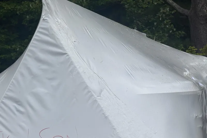 Slide: The Image of White tent with visible creases, set against a backdrop of green foliage. - 13