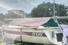 Slide: The Image of 1979 O'Day 19 sailboat with cover, docked outdoors under a cloudy sky. - 2