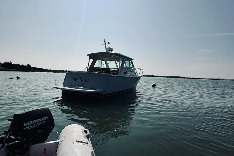 Slide: The Image of 2013 Back Cove 30 boat named "Sisters" on calm water, with Mercury engine nearby. - 64