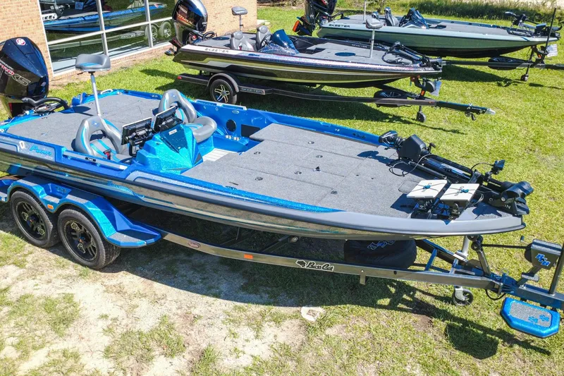 Slide: The Image of 2025 Bass Cat Puma STS boat, blue, parked on grass, with trailer and fishing equipment. - 2