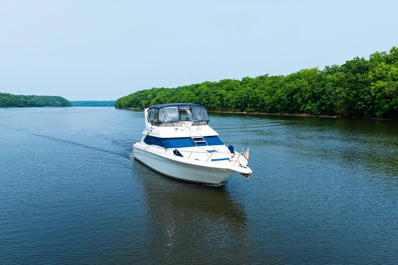 The Image of 1995 Sea Ray 440 Express Bridge cruising on a scenic lake with waterfront homes. - 0