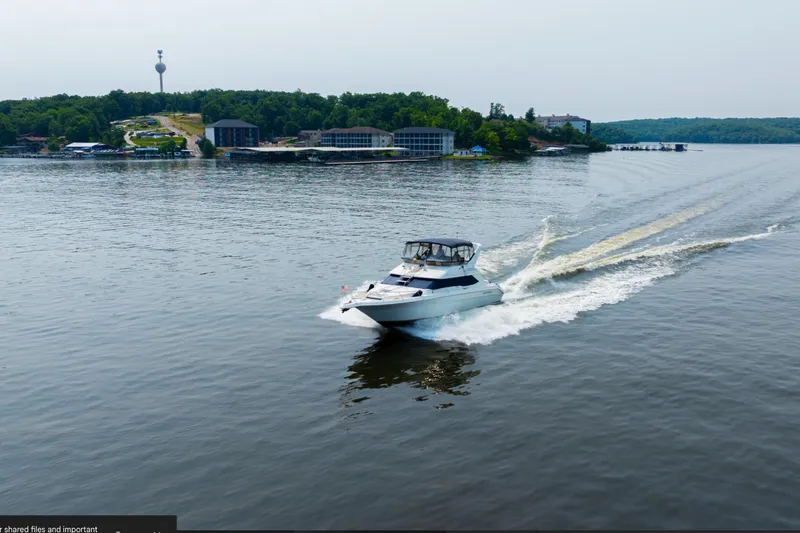 Slide: The Image of A 1995 Sea Ray 440 Express Bridge yacht cruising on a serene lake surrounded by lush greenery. - 2