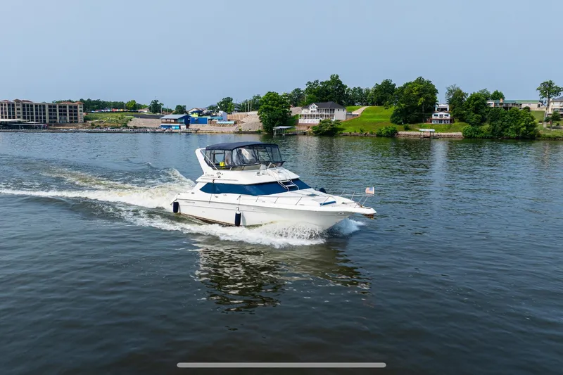 Slide: The Image of 1995 Sea Ray 440 Express Bridge cruising on a scenic lake with shoreline view. - 3