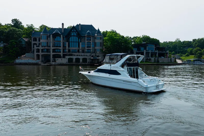 Slide: The Image of Sea Ray 440 Express Bridge yacht on a serene lake, with luxurious waterfront homes in the background. - 4