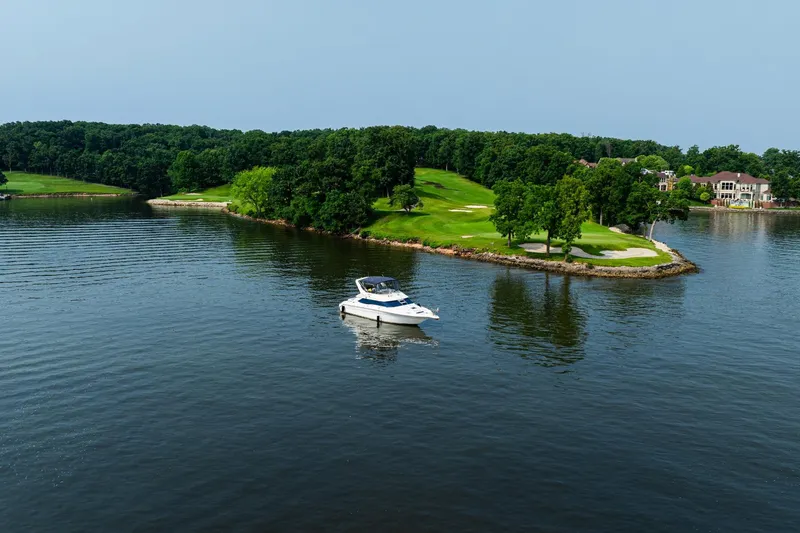 Slide: The Image of 1995 Sea Ray 440 Express Bridge yacht on serene lake near lush green island. - 5