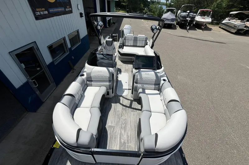 Slide: The Image of 2025 Avalon Excalibur Versatile boat with rear bench and windshield, parked outdoors. - 9