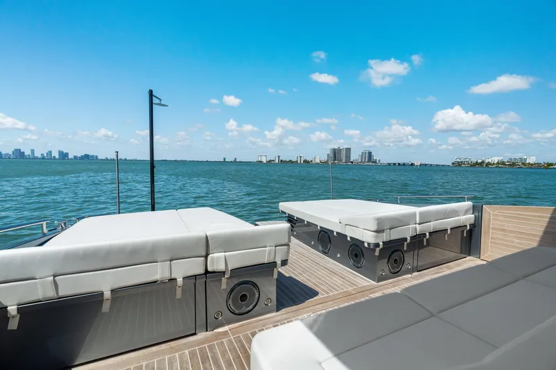 Slide: The Image of 2024 CNM CONTINENTAL 54 SuperSport yacht deck with sunbeds, overlooking ocean and city skyline. - 24