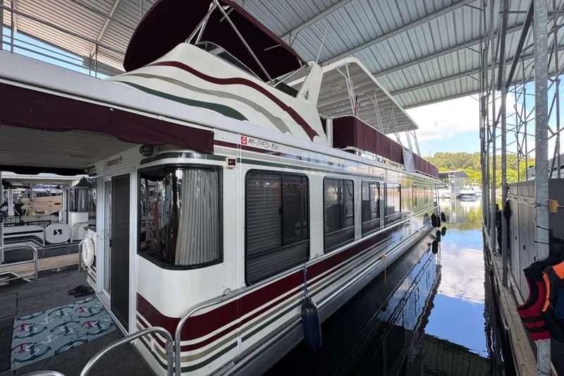 The Image of 2002 Sumerset houseboat on a river, under a bridge, with American flags and lush greenery. - 0