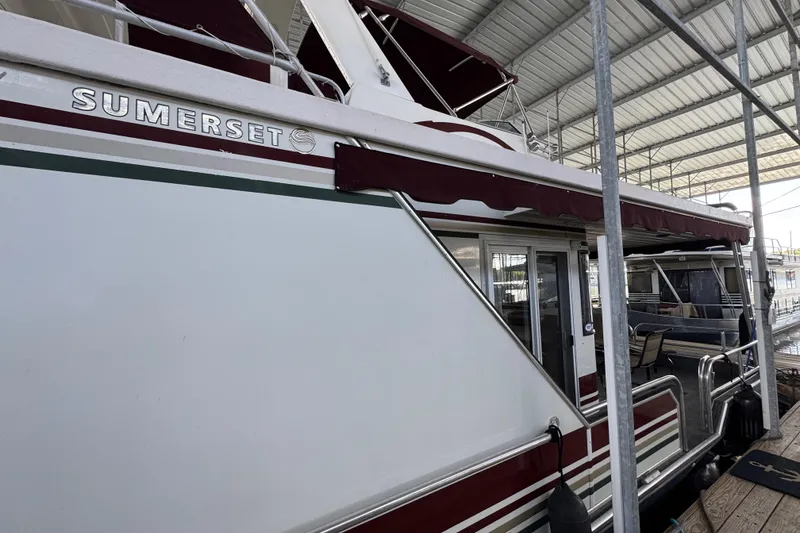 Slide: The Image of 2002 Sumerset houseboat on a serene lake, featuring American flags and outdoor seating. - 3