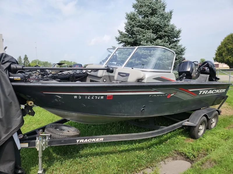 Slide: The Image of 2019 Tracker Targa V-18 Combo boat on trailer, parked on grass with trees in background. - 3