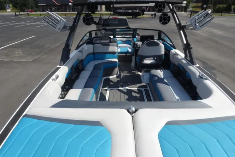 Slide: The Image of 2016 Malibu 25 LSV boat interior with blue and white seating, parked outdoors. - 6