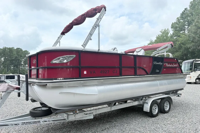 Slide: The Image of 2022 Bentley Pontoons 223 Elite on trailer, red and silver design, parked outdoors. - 3