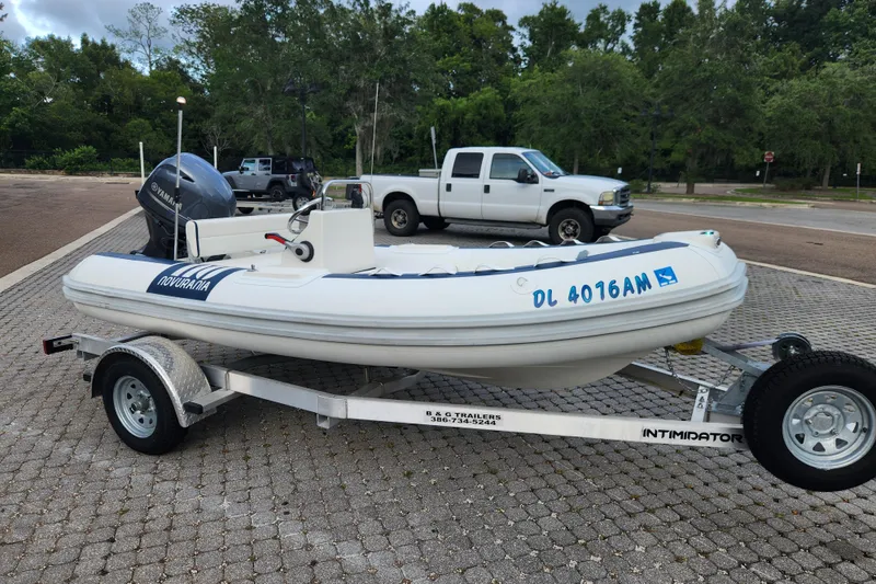 Slide: The Image of 2019 Novurania DL 400 boat on trailer, parked in a lot with trees in background. - 6