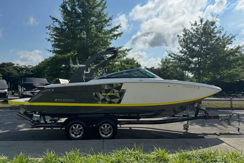 Slide: The Image of 2017 Four Winns TS242 boat on trailer, parked outdoors with trees in background. - 3