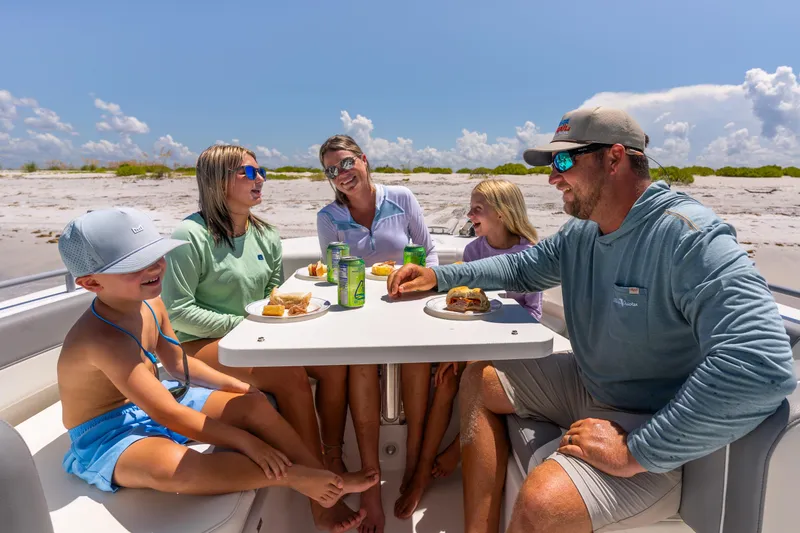 Slide: The Image of Family enjoying a meal on a 2026 Edgewater 250 CC boat by the beach. - 10