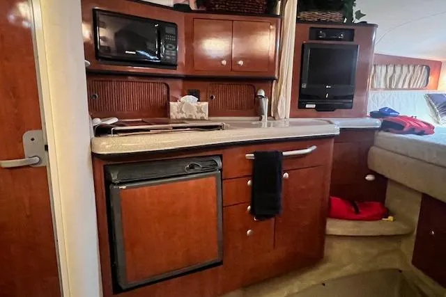 Slide: The Image of 2006 Sea Ray 300 Sundancer interior kitchen with microwave, fridge, and wood cabinetry. - 18