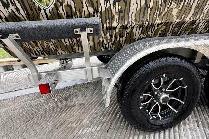 Slide: The Image of Trailer with camo-patterned Avid 20 Rogue boat, 2024 model, on textured pavement. - 10