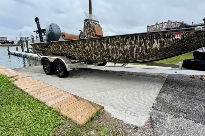 Slide: The Image of 2024 Avid 20 Rogue boat on trailer at boat ramp, camo design, overcast sky. - 9
