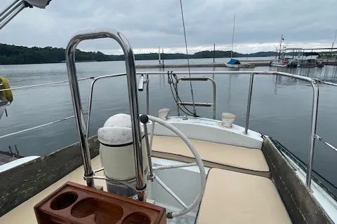 Slide: The Image of 1976 Ranger 33 sailboat deck with steering wheel, docked on a calm lake under cloudy skies. - 7