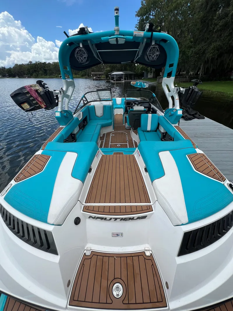 Slide: The Image of 2018 Nautique Super Air G23 boat with vibrant blue and white design docked by a serene lake. - 7