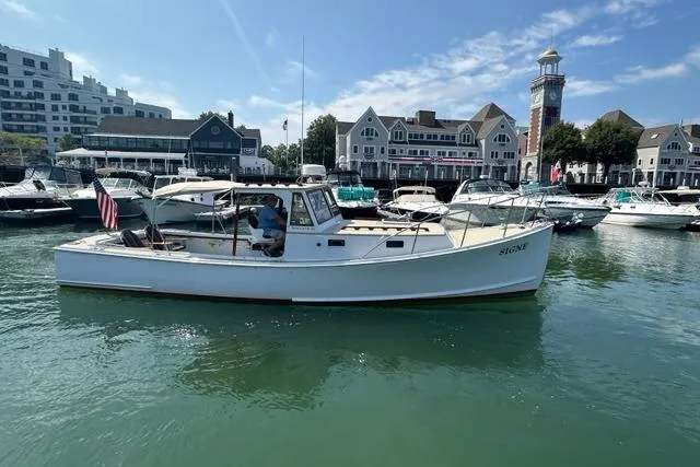Slide: The Image of 1987 Holland 32 boat docked in a marina with waterfront buildings and a lighthouse. - 6