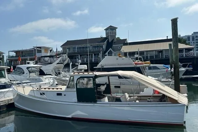 Slide: The Image of 1987 Holland 32 boat docked at a marina with other vessels and buildings in the background. - 7