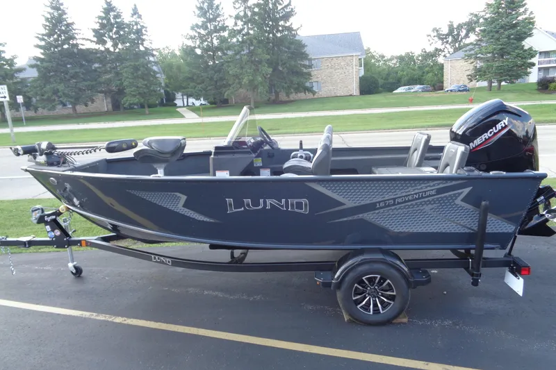 Slide: The Image of 2025 Lund 1675 Adventure SS boat with Mercury engine on trailer, parked outdoors. - 4