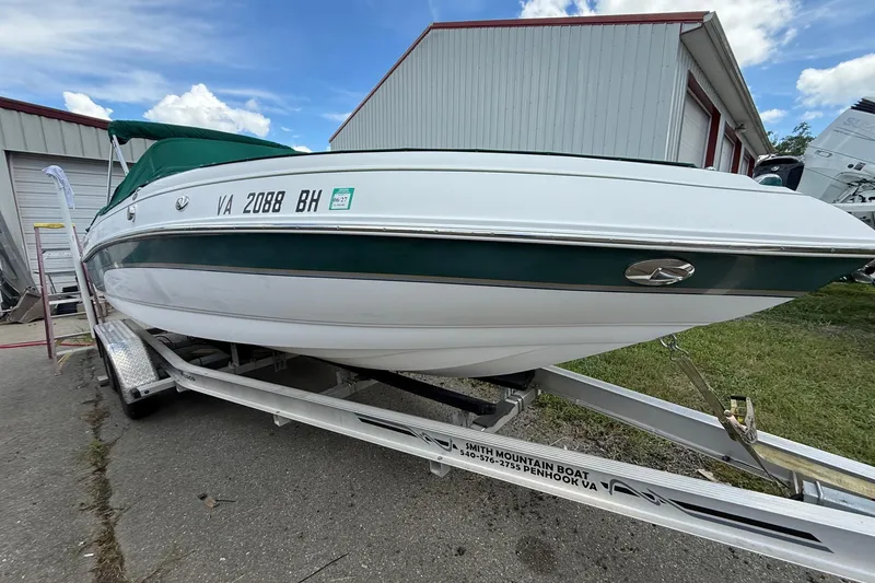 Slide: The Image of 2005 Bryant 214 boat on trailer, green and white, parked near a building. - 2