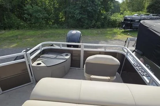 Slide: The Image of 2025 Sun Tracker Sportfish™ 20 DLX pontoon boat interior with seating and motor, surrounded by greenery. - 7