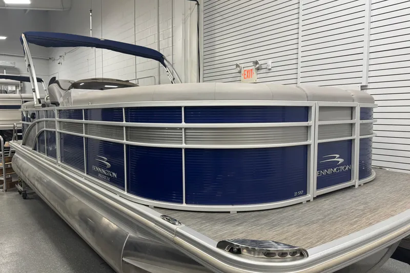 Slide: The Image of 2020 Bennington 23 SXPD pontoon boat in showroom, featuring sleek blue and silver design. - 1