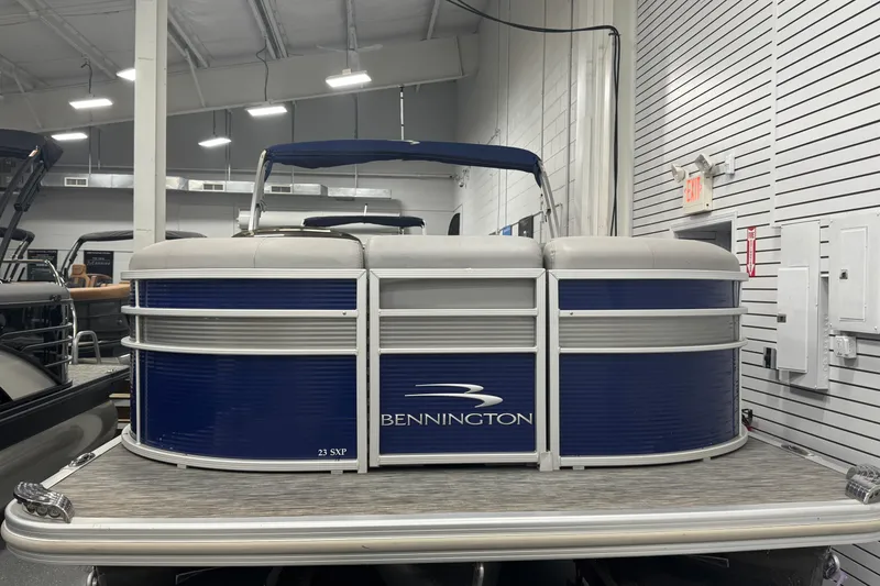 Slide: The Image of 2020 Bennington 23 SXPD pontoon boat in showroom, featuring blue and white design. - 2