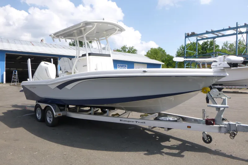 Slide: The Image of 2024 Ranger 2660 Bay boat on trailer, parked outdoors near a blue building. - 2