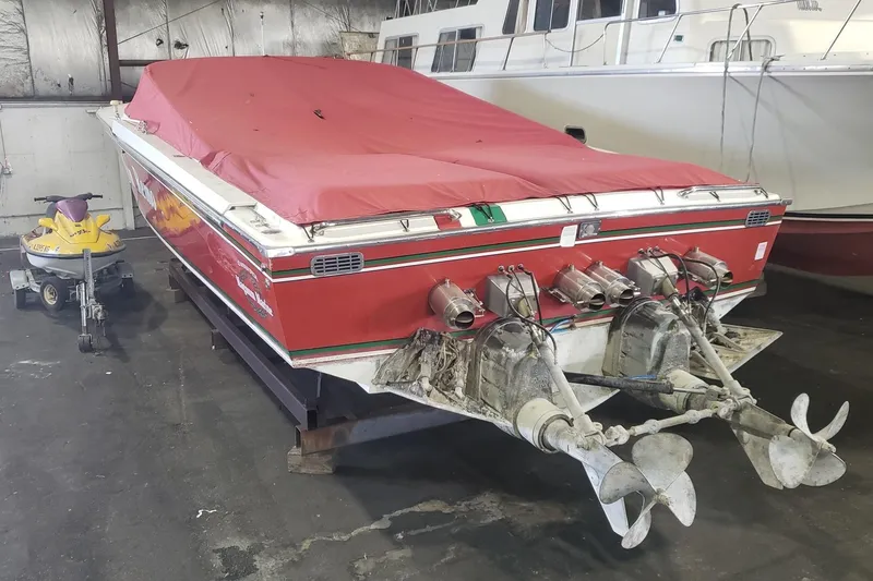 Slide: The Image of Red 1982 Magnum 40 boat with covered deck, dual propellers, and nearby yellow jet ski in storage. - 3