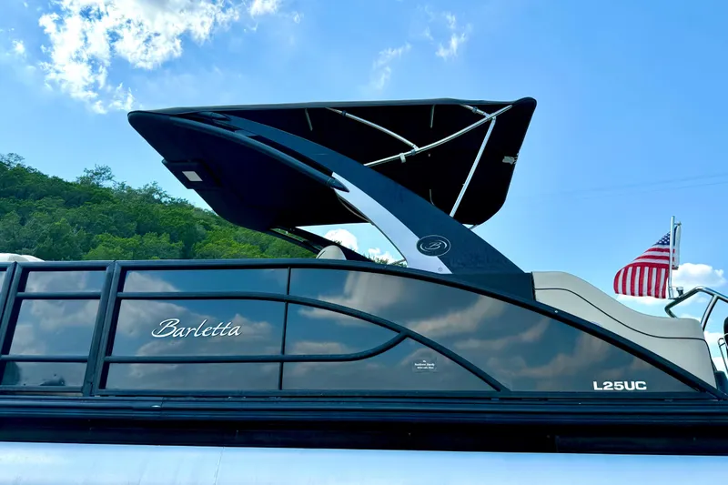 Slide: The Image of 2021 Barletta L25UC pontoon boat with canopy, American flag, and scenic background. - 10