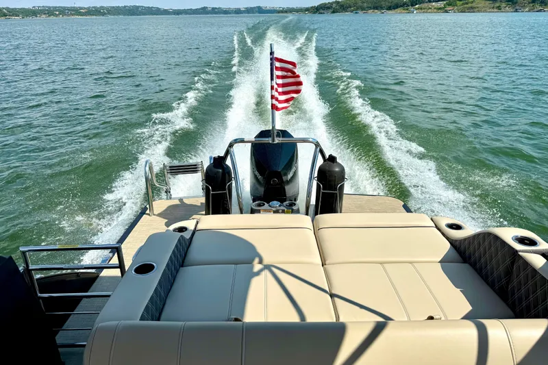 Slide: The Image of 2021 Barletta L25UC pontoon boat cruising on a lake with American flag waving. - 13