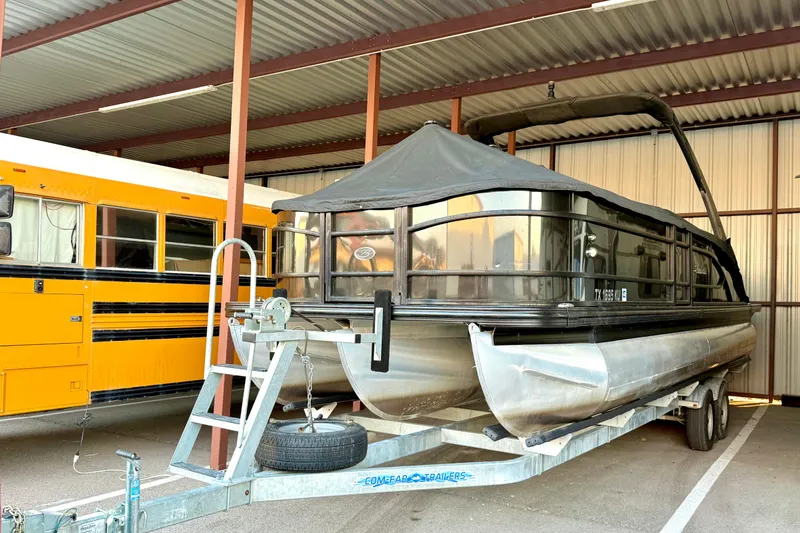 Slide: The Image of 2021 Barletta L25UC pontoon boat on trailer, parked in covered storage next to a yellow bus. - 22
