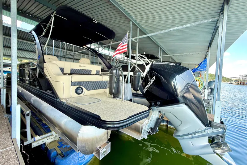 Slide: The Image of 2021 Barletta L25UC pontoon boat with Mercury engine docked under a covered marina. - 25