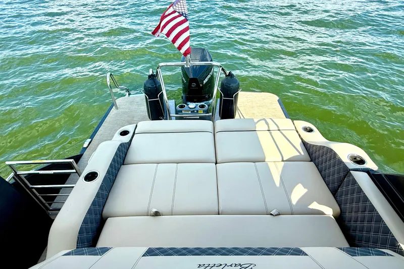 Slide: The Image of 2021 Barletta L25UC pontoon boat with American flag, spacious seating, and scenic water view. - 27