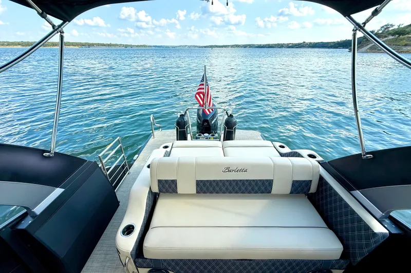 Slide: The Image of 2021 Barletta L25UC pontoon boat on a serene lake with American flag. - 39