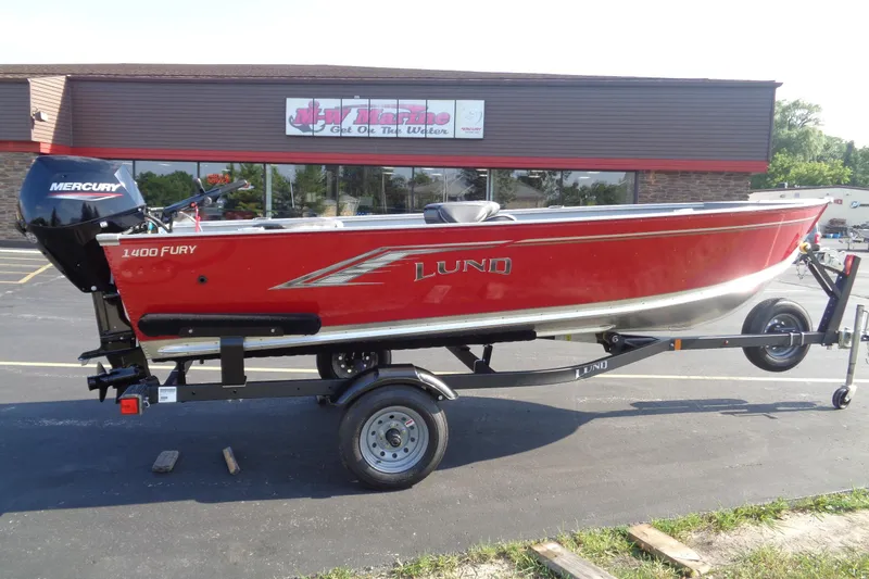 Slide: The Image of 2026 Lund 1400 Fury Tiller boat in red on a trailer, parked outside a store. - 5