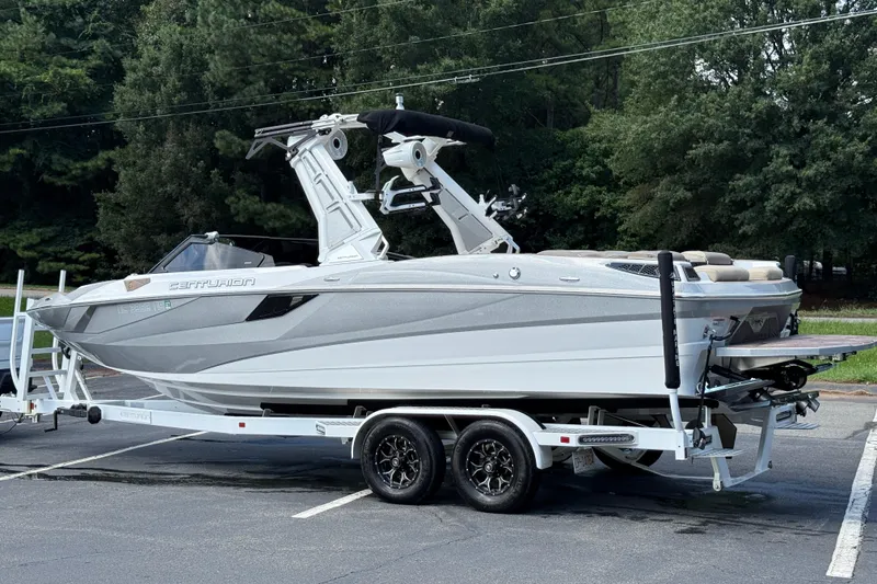 Slide: The Image of 2023 Centurion Fi25 boat on trailer in parking lot, surrounded by trees. - 20