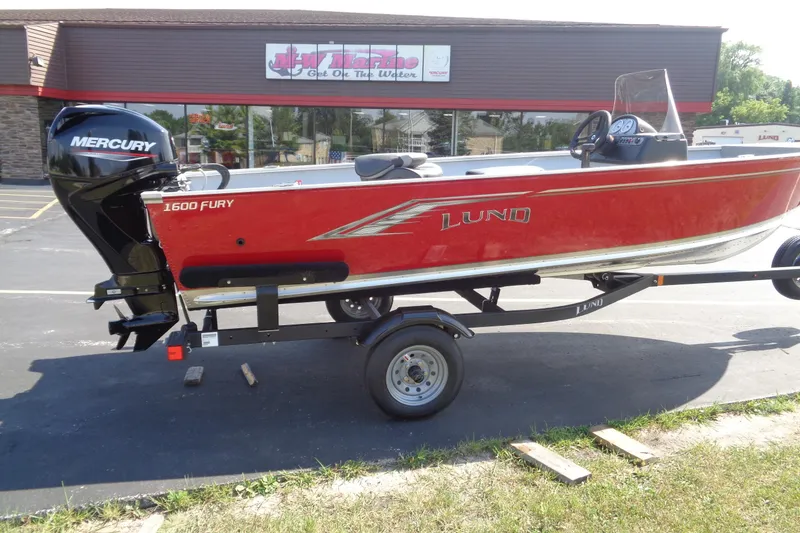 Slide: The Image of 2026 Lund 1600 Fury SS boat on trailer, red exterior, Mercury engine, parked outside a store. - 7