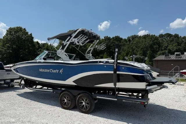 Slide: The Image of 2016 MasterCraft X26 boat on trailer, blue and white, parked outdoors under clear sky. - 10