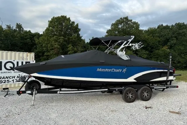 Slide: The Image of 2016 MasterCraft X26 boat on trailer, covered, parked outdoors with trees in background. - 25