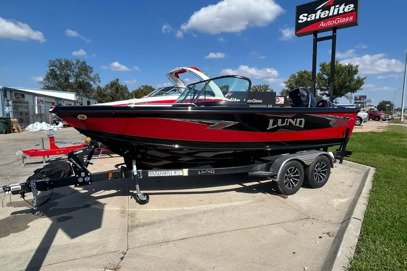 Slide: The Image of 2026 Lund 1875 Tyee boat in red and black on a trailer, parked outdoors. - 9